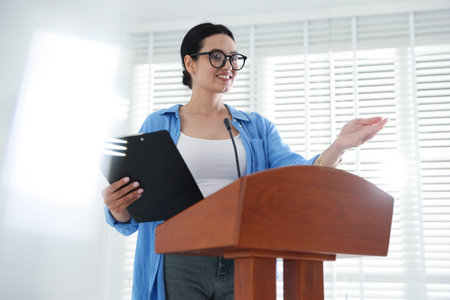 Woman giving public speech with microphone at lectern indoorsの写真素材