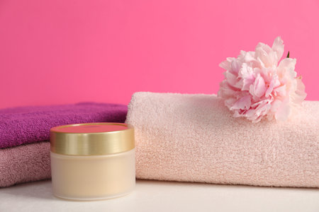 Soft towels, cosmetic product and peony flower on white table against pink background, closeupの写真素材