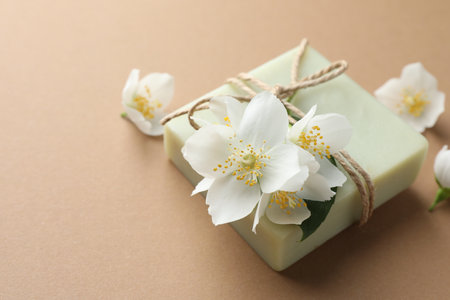 Soap bar and jasmine flowers on light brown background, closeup. Space for textの写真素材