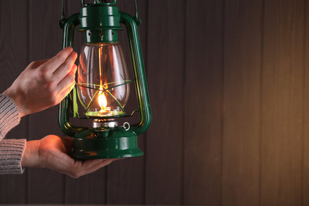 Man with vintage kerosene lamp on wooden background, closeup. Space for textの写真素材