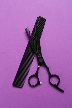 Scissors and comb on violet background, flat lay. Hairdresser's toolsの写真素材