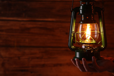 Man with vintage kerosene lamp on wooden background, closeup. Space for textの写真素材