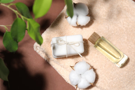Soap bars, cosmetic product, towel and cotton flowers on brown background, top viewの写真素材