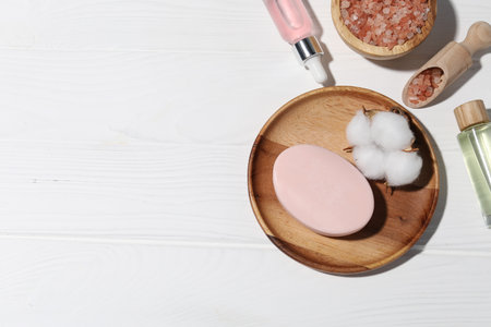 Soap bar, cosmetic products and cotton flower on white wooden table, flat lay. Space for textの写真素材