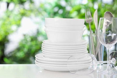 Different clean dishes on white table against blurred green backgroundの写真素材