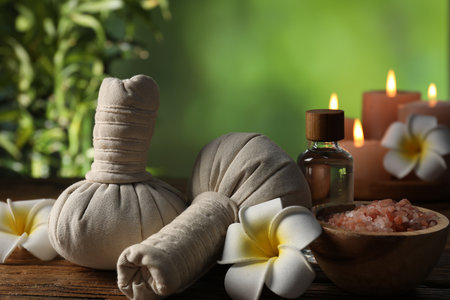 Spa composition with herbal bags and cosmetic products on wooden table against blurred green background, closeupの写真素材