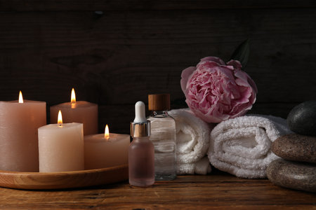 Spa composition with cosmetic products, burning candles and flower on wooden table against black background, closeupの写真素材