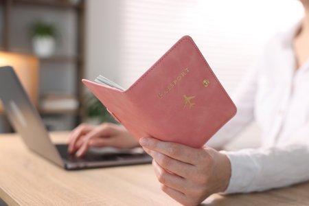 Woman with passport using laptop at table indoors, closeupの写真素材