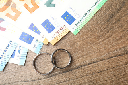 Silver wedding rings and euro banknotes on wooden table, flat lay. Space for textの写真素材
