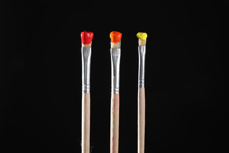 Three brushes with color paints on black background, closeup