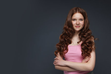Portrait of beautiful teenage girl with healthy wavy hair on dark grey background. Space for textの写真素材