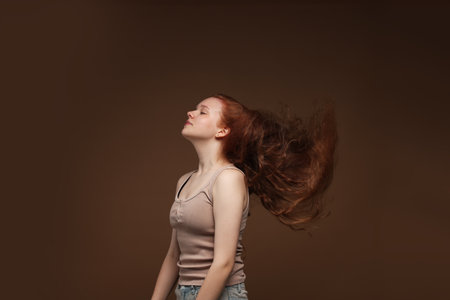 Teenage girl with healthy wavy hair on brown backgroundの写真素材