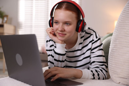 Teenage student in headphones using laptop while studying on sofa at homeの写真素材