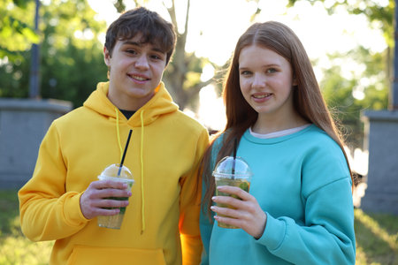 Teenage girl and boy with drinks in parkの写真素材