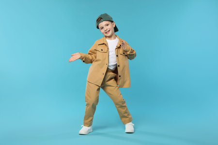 Happy little boy in baseball hat dancing on light blue background