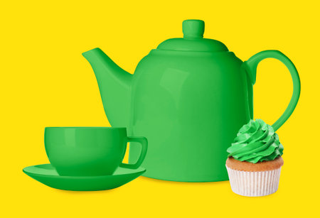 Green teapot, cup and cupcake against yellow backgroundの写真素材
