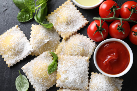 Uncooked ravioli, sauce, tomatoes and basil on black table, flat layの写真素材