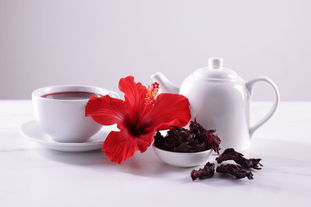 Tasty hibiscus tea, dry roselle sepals and beautiful flower on white table against gray backgroundの写真素材