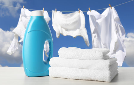 Fabric softener and towels on table outdoors. Clothes drying against skyの写真素材