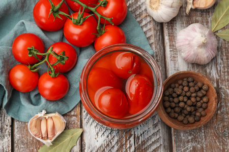 Tasty pickled tomatoes in jar and ingredients on wooden table, flat layの写真素材