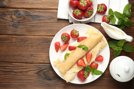 Tasty crepes with cream, strawberries and mint on wooden table, flat lay. Space for textの写真素材