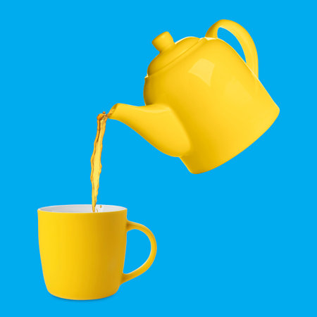 Pouring tea from yellow teapot into cup against blue backgroundの写真素材
