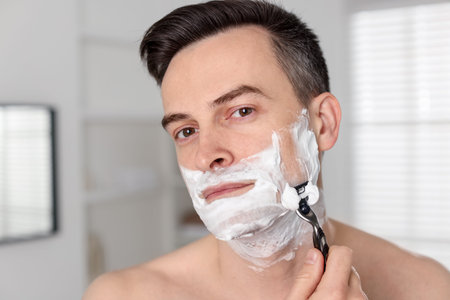 Handsome man shaving with razor at homeの写真素材