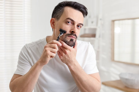 Handsome man shaving with razor in bathroomの写真素材