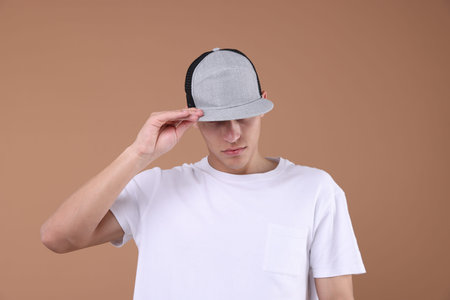 Young man wearing stylish baseball hat on light brown background