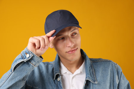Young man in stylish baseball hat on orange backgroundの写真素材