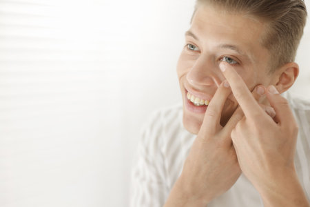 Man putting in contact lens at home. Space for textの写真素材