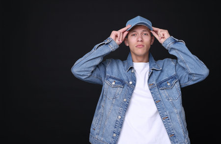 Young man wearing stylish denim baseball hat on black background, space for textの写真素材