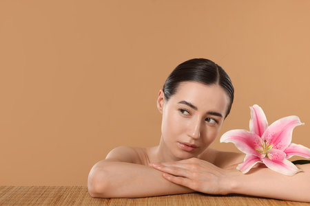 Beautiful woman after spa treatment with lily flower at bamboo table on beige background. Space for textの写真素材