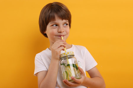 Cute little boy drinking lemonade on orange background. Refreshing drinkの写真素材