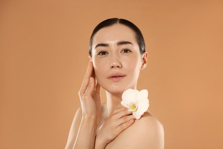 Beautiful woman after spa treatment with orchid flower on beige backgroundの写真素材