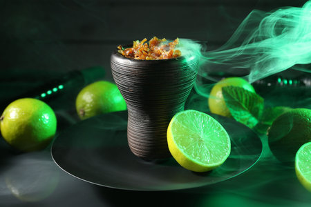 Hookah bowl with limes, mint and smoke on black table, closeup