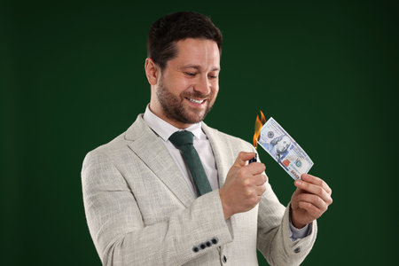 Greedy businessman burning dollar banknote with lighter on dark green backgroundの写真素材