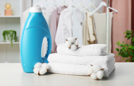 Fabric softener, towels and cotton flowers on table against rack with clothes in roomの写真素材