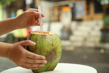 Woman with green coconut of refreshing drink at table outdoors, closeup. Space for textの写真素材