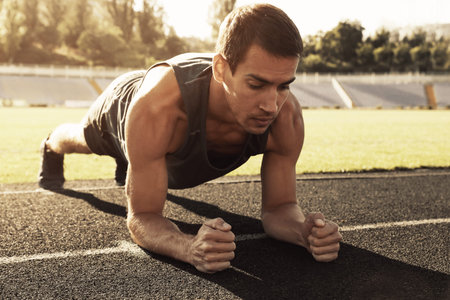 Sporty man doing plank exercise at stadium