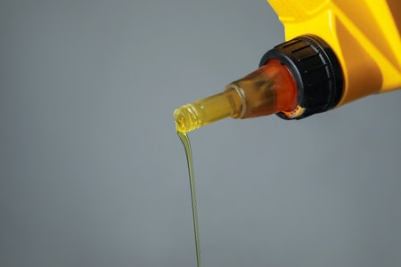 Pouring motor oil from yellow canister on gray background, closeup. Space for textの写真素材