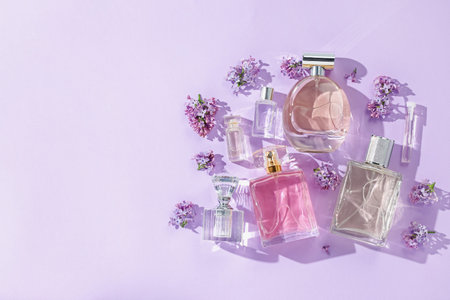 Luxury perfumes and beautiful lilac flowers on light violet background, flat lay. Space for text