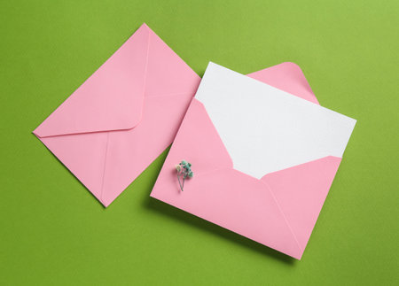 Blank invitation card and envelopes on green background, flat lay. Space for designの写真素材