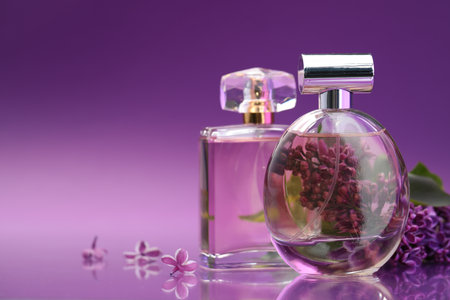 Bottles with perfumes and lilac flowers on mirror surface against color gradient background, closeup. Space for textの写真素材