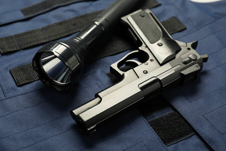 Flashlight and black gun on bulletproof vest, above view. Police equipment