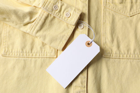 Cardboard tag on pale yellow shirt, top viewの写真素材