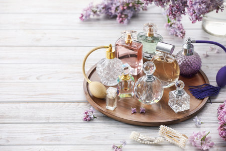 Bottles of perfumes, accessories and lilac flowers on white wooden table. Space for text
