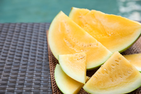 Pieces of ripe yellow watermelon on wicker table near swimming pool, closeup. Space for textの写真素材