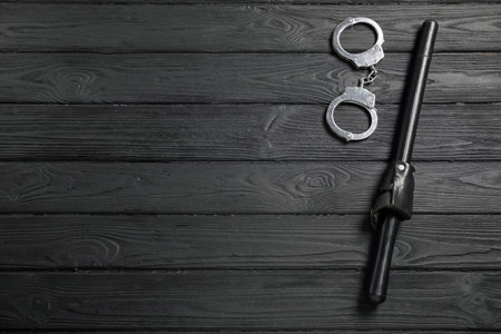 Police baton and handcuffs on black wooden table, flat lay. Space for textの写真素材