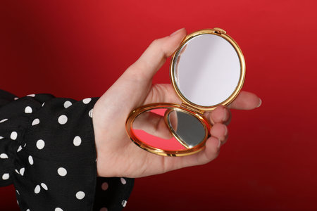Woman holding open pocket mirror on red background, closeupの写真素材